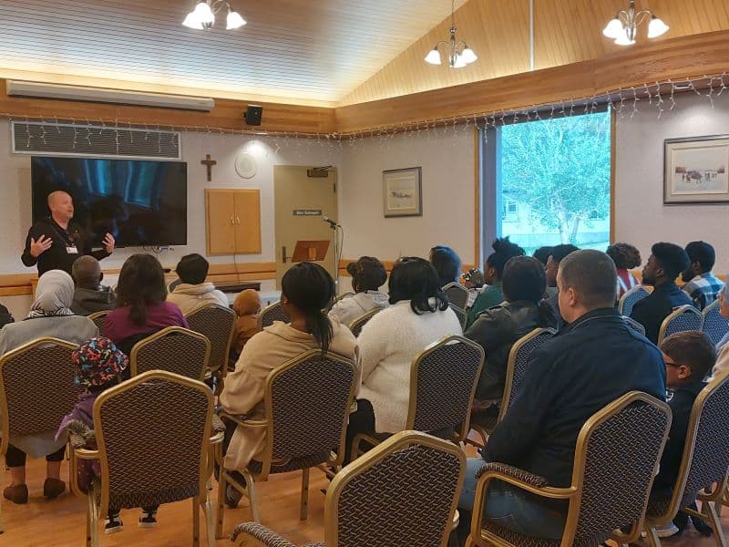 Les participants au rural vous parle sont assis dans une salle et écoute la présentation du directeur de la Villa Youville debout en avant.